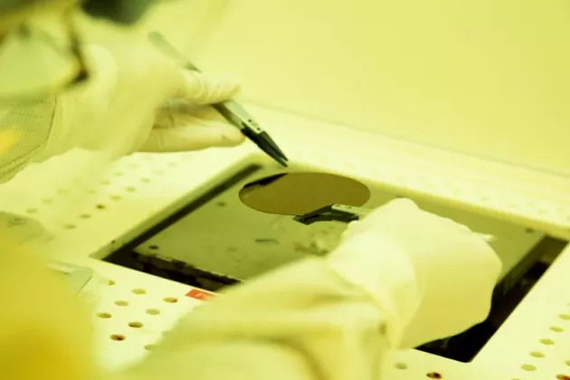 A person wearing protective gloves uses a tool to handle a semiconductor wafer in a cleanroom environment contributing to PhD and postdoctoral projects.