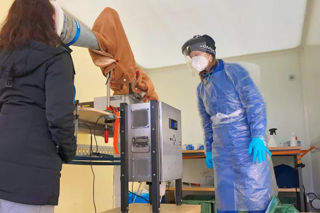 Two people in a laboratory room, one of them wearing protective clothing.