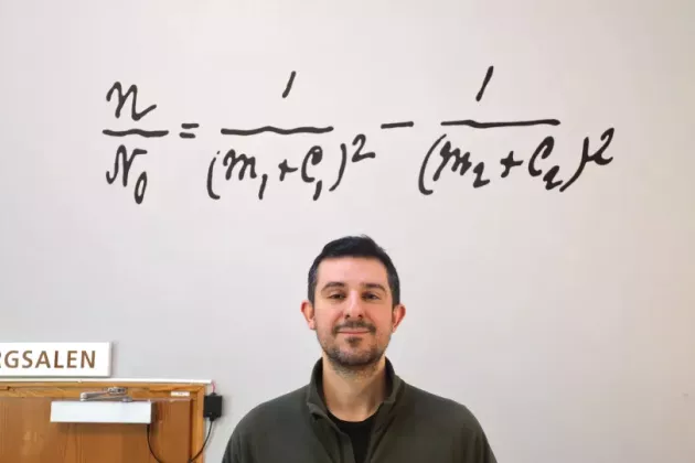 Photo of a man standing in front of a wall with the Rydberg formula written on it.