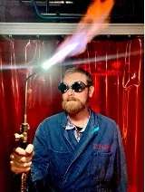 Photo of a man wearing goggles and a welding torch.